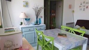 Zona de menjador amb taula i cadires, un televisor fixat a la paret, i una cuina amb armaris i microones.