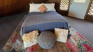 Ein gemütliches Schlafzimmer im Dachgeschoss mit Holzbalkendecke, einem Bett mit gemustertem Überwurf, Kissen und einem farbenfrohen Teppich.