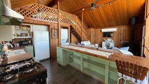 Ein gemütliches Blockhaus mit einer Küche, die einen Herd, ein Waschbecken und einen Kühlschrank beinhaltet. Es gibt einen Essbereich mit einer Bank und einem Kamin.