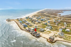 An aerial view of a coastal residential area with houses, a beach, and a pier.