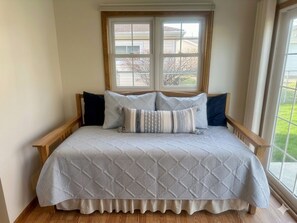 Una cama con cubrecolcha blanco acolchado, cabecera de madera y dos ventanas arriba.
