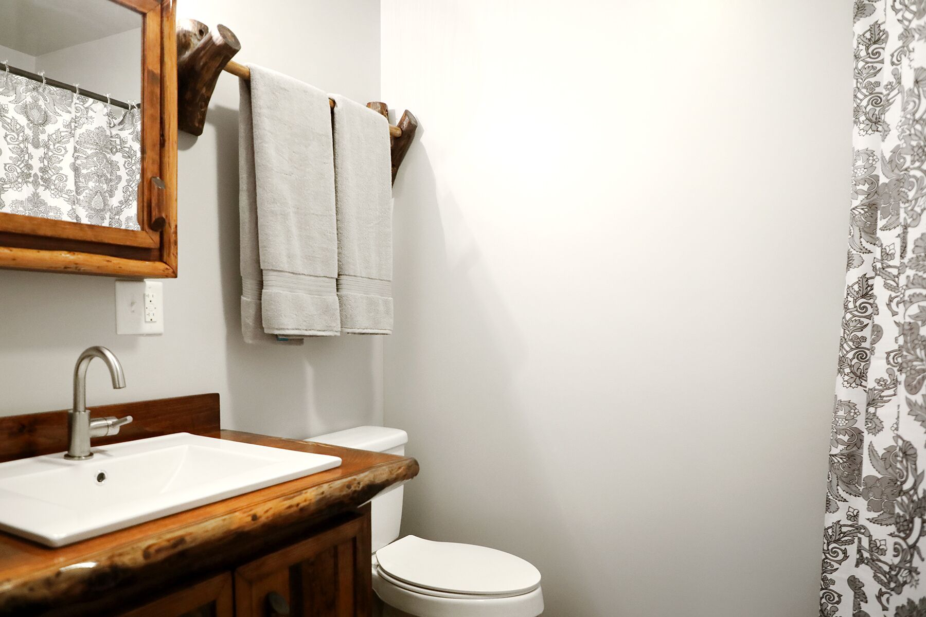 A bathroom with a wooden vanity, a white sink, a toilet, and a mirror with a towel hanging on the wall.