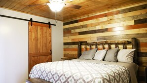 A bedroom with a wooden slat wall, a bed with patterned bedding, a wooden bench, and a ceiling fan.