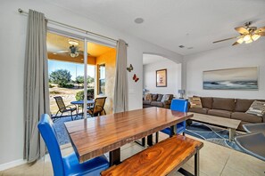 Un salón espacioso con una mesa de comedor de madera, sillas azules, un sofá marrón y un ventilador de techo.