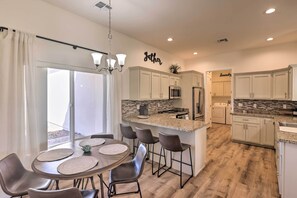 Una cocina moderna con armarios blancos, encimera de granito y un comedor con una mesa redonda y taburetes de bar.