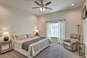 A bedroom with a bed, nightstands, a ceiling fan, a window with curtains, a chair, and a TV mounted on the wall. - Bright Home w/ Yard, 4 Mi to Colorado River! (Fort Mohave)