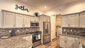 Una cocina moderna con armarios blancos, encimeras de granito, electrodomésticos de acero inoxidable y una salpicadura con diseño de mosaico.