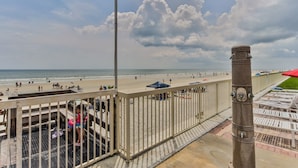 Blick auf einen Strand vom Balkon mit Geländer, einem Metallpfosten und Strandstühlen.