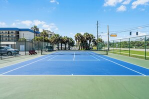 Un court de tennis en plein air, doté d’un filet, entouré d’une clôture et muni d’un banc.