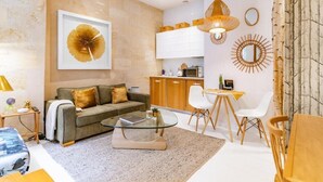 Ein modernes Wohnzimmer mit Sofa, Couchtisch und Essbereich. Im Hintergrund ist eine Küche mit Schränken und einer Mikrowelle zu sehen.