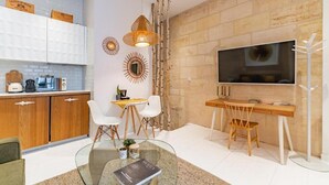 Eine moderne Küche mit weißen Schränken, ein Essbereich mit einem Glastisch und ein an einer Steinwand befestigter Fernseher.