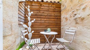 Eine kleine Terrasse mit zwei weißen Metallstühlen und einem runden Tisch, vor einer rustikalen Holzwand.