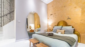 Ein Schlafzimmer mit einem Bett, zwei hölzernen Hocker, einem Nachttisch, einer Lampe und einer Wand mit Struktur.