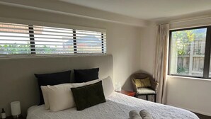 Una cama bien hecha con colcha blanca, dos toallas enrolladas y una silla de mimbre con cojín.