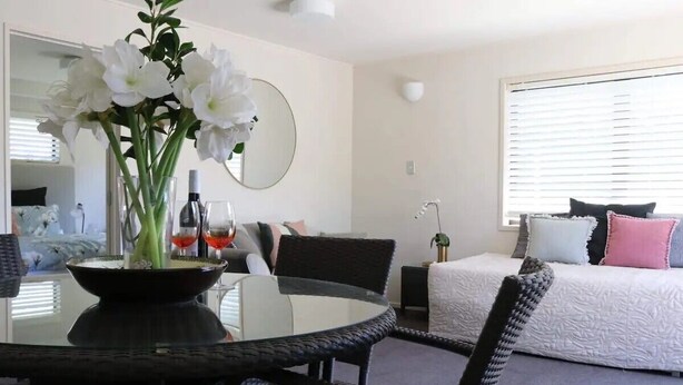 Una habitación moderna con una mesa de comedor, sillas, una cama con almohadas, un espejo y una ventana con persianas.