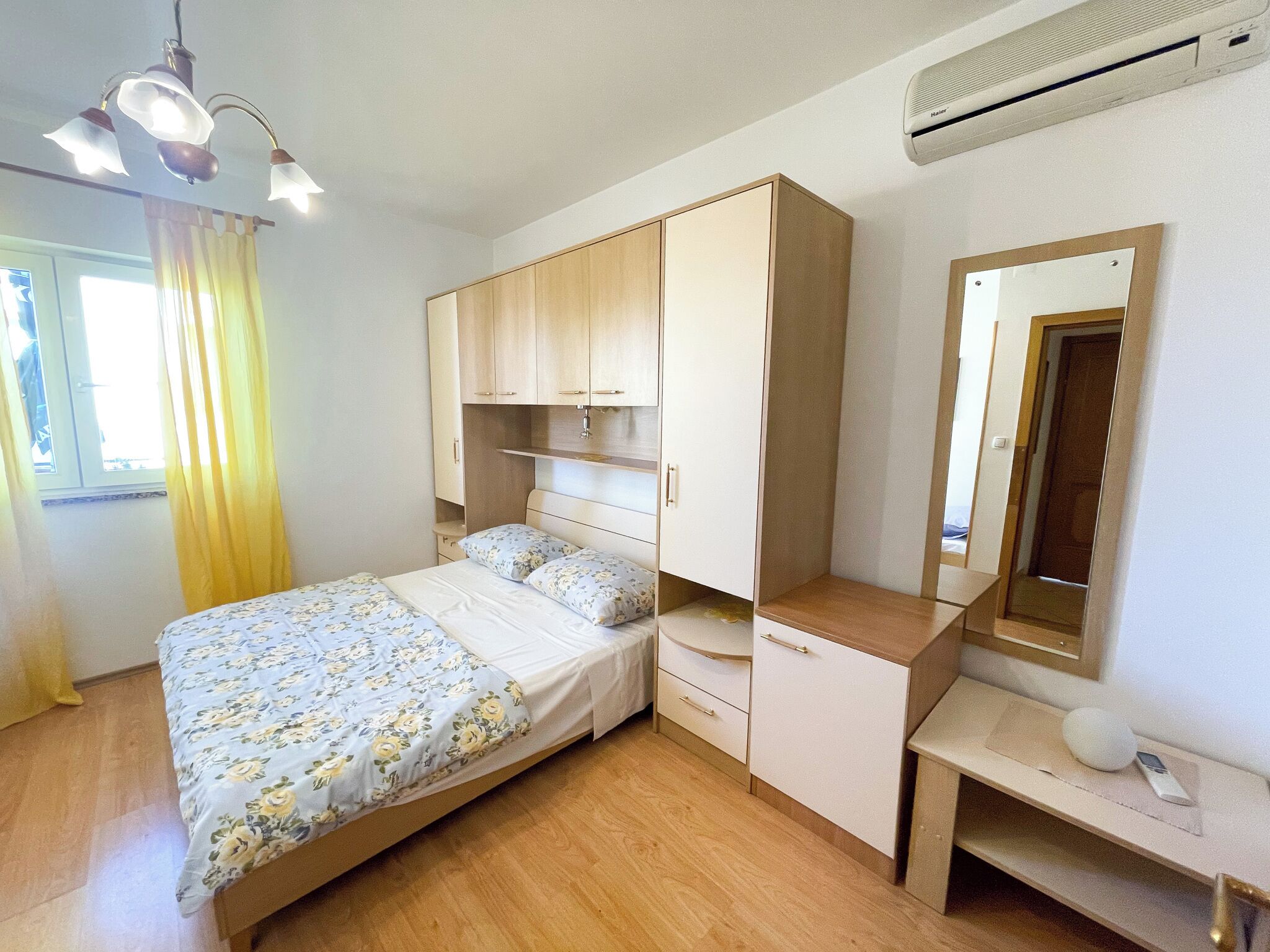 Een slaapkamer met een bed, een houten garderobe, een nachtkastje en een spiegel.