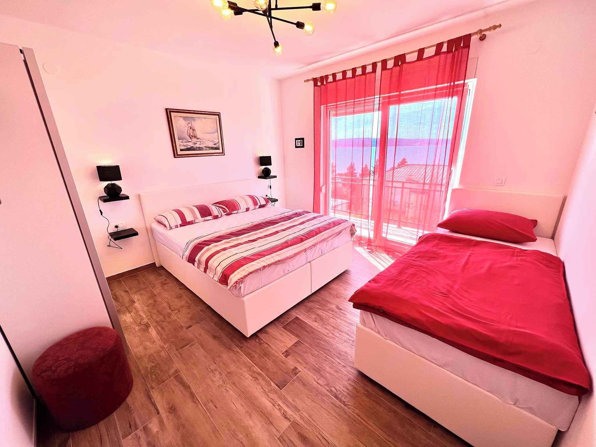 A bedroom with a bed, a smaller bed, a nightstand, a lamp, a picture on the wall, and a window with curtains.