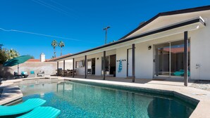 Uma área de piscina moderna com água cristalina, espreguiçadeiras e um terraço coberto.