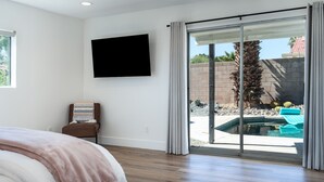 Quarto com cama, TV fixada na parede e porta de vidro deslizante para área da piscina.