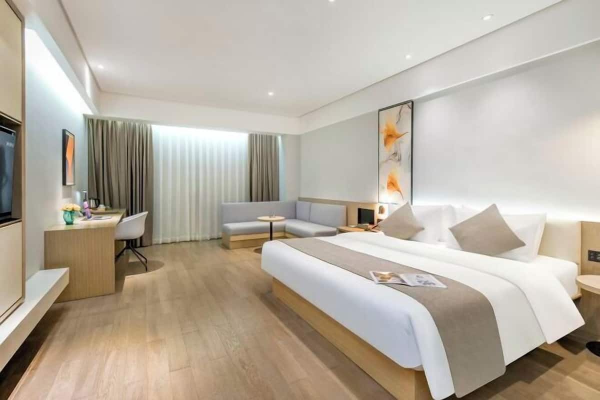 A modern hotel room with a large bed, a desk, a sofa, and a television.