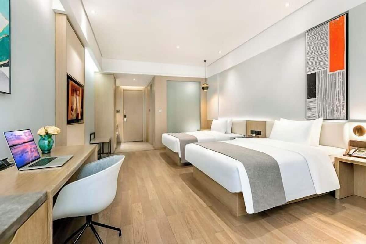 A modern hotel room with a desk, two beds, a chair, and artwork on the walls.