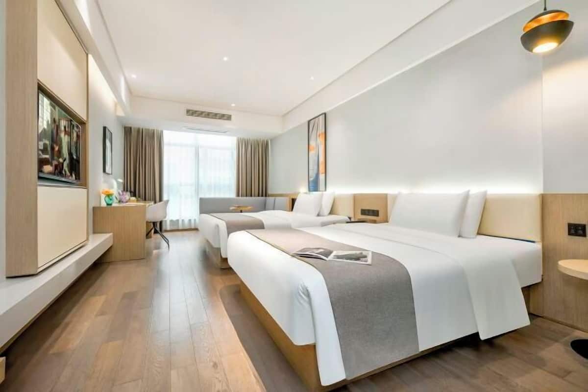 A hotel room with two beds, a desk, a chair, a TV, and a window.
