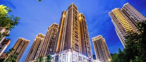 Un edificio alto con varios pisos, rodeado de árboles y otros edificios.