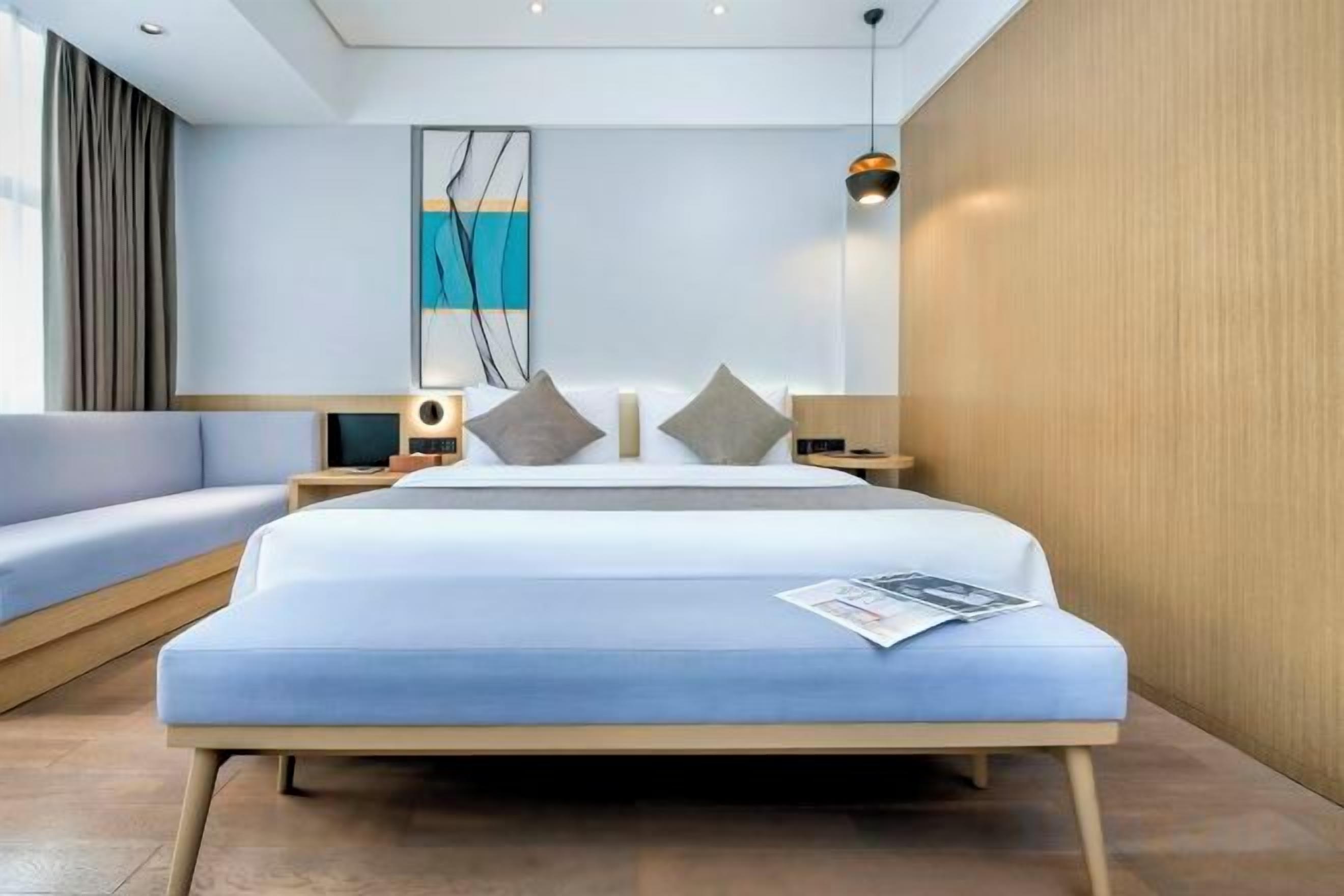 Una habitación de hotel moderna con una cama grande, un sofá, una mesita de noche con lámpara y una obra de arte colgada en la pared.