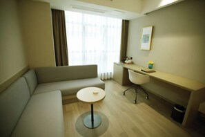 A modern hotel room with a sofa, a small round table, a desk with a chair, and a window with curtains. - Saint Hotel (Chongqing)