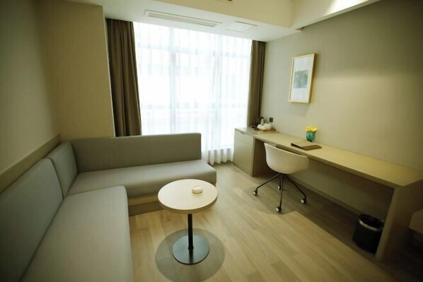 A modern hotel room with a sofa, a small round table, a desk with a chair, and a window with curtains. - Saint Hotel (Chongqing)