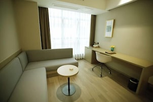 Una habitación de hotel moderna con sofá, una mesita redonda, un escritorio con silla y una ventana con cortinas.