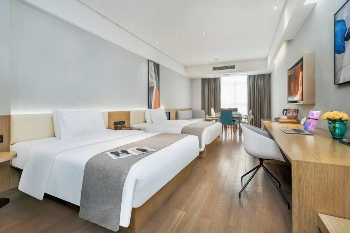 A hotel room with two beds, a desk, a chair, and a large window.