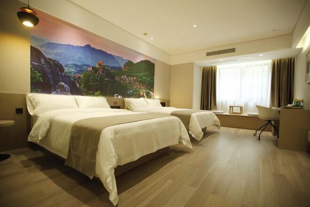 A hotel room with two beds, a desk, a chair, and a large mural on the wall.