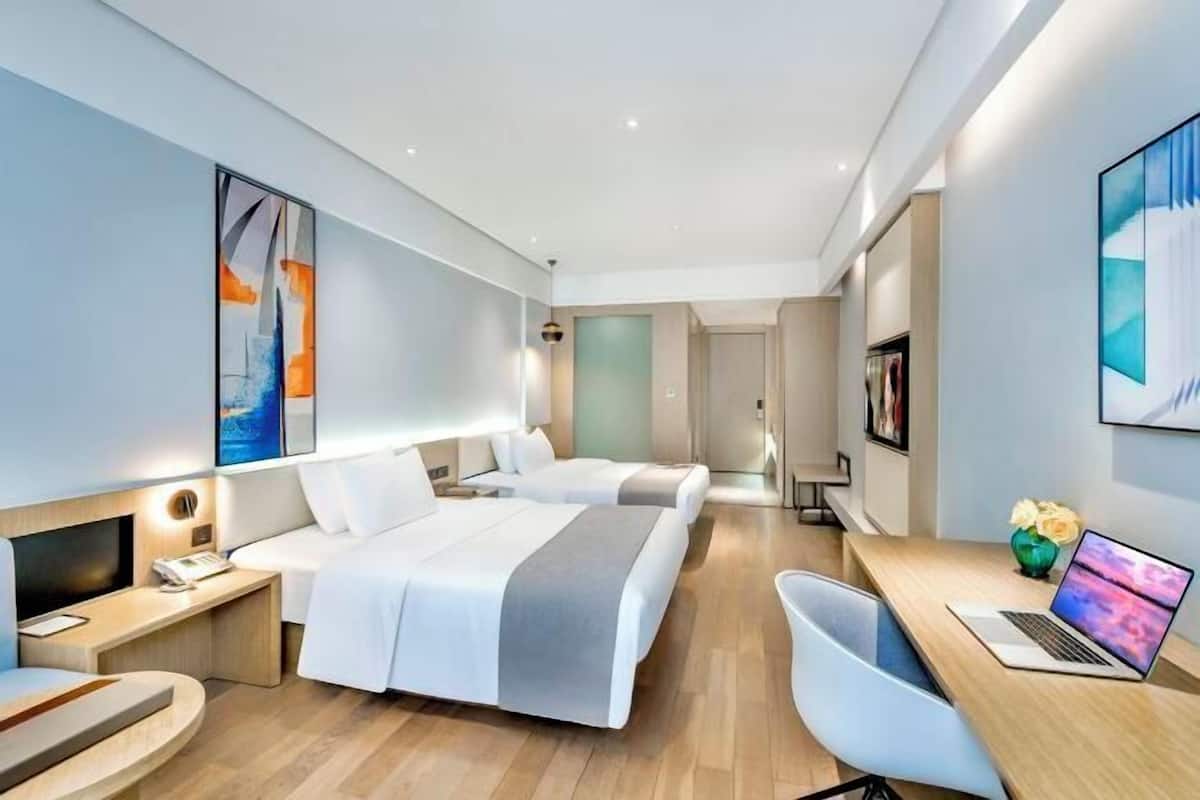 A modern hotel room with two beds, a desk with a laptop, a TV, and artwork on the walls.