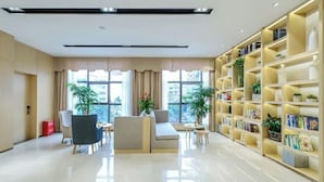 A modern living room with a sofa, chairs, a coffee table, and a bookshelf filled with books and decorative items. - Saint Hotel (Chongqing)