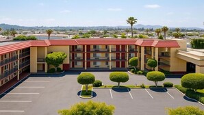 A multi-story hotel with a red roof, a parking lot, and neatly trimmed trees. - Rancho San Diego Inn & Suites (El Cajon)