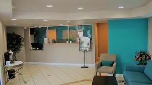A reception area with a counter, seating, and a potted plant. - Rancho San Diego Inn & Suites (El Cajon)