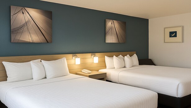 A hotel room with two beds, a wooden headboard, bedside lamps, and artwork on the walls. - Rancho San Diego Inn & Suites (El Cajon)