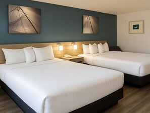 A hotel room with two beds, a wooden headboard, bedside lamps, and artwork on the walls.