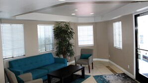 A living room with a blue sofa, a grey armchair, a coffee table, and a large plant. - Rancho San Diego Inn & Suites (El Cajon)