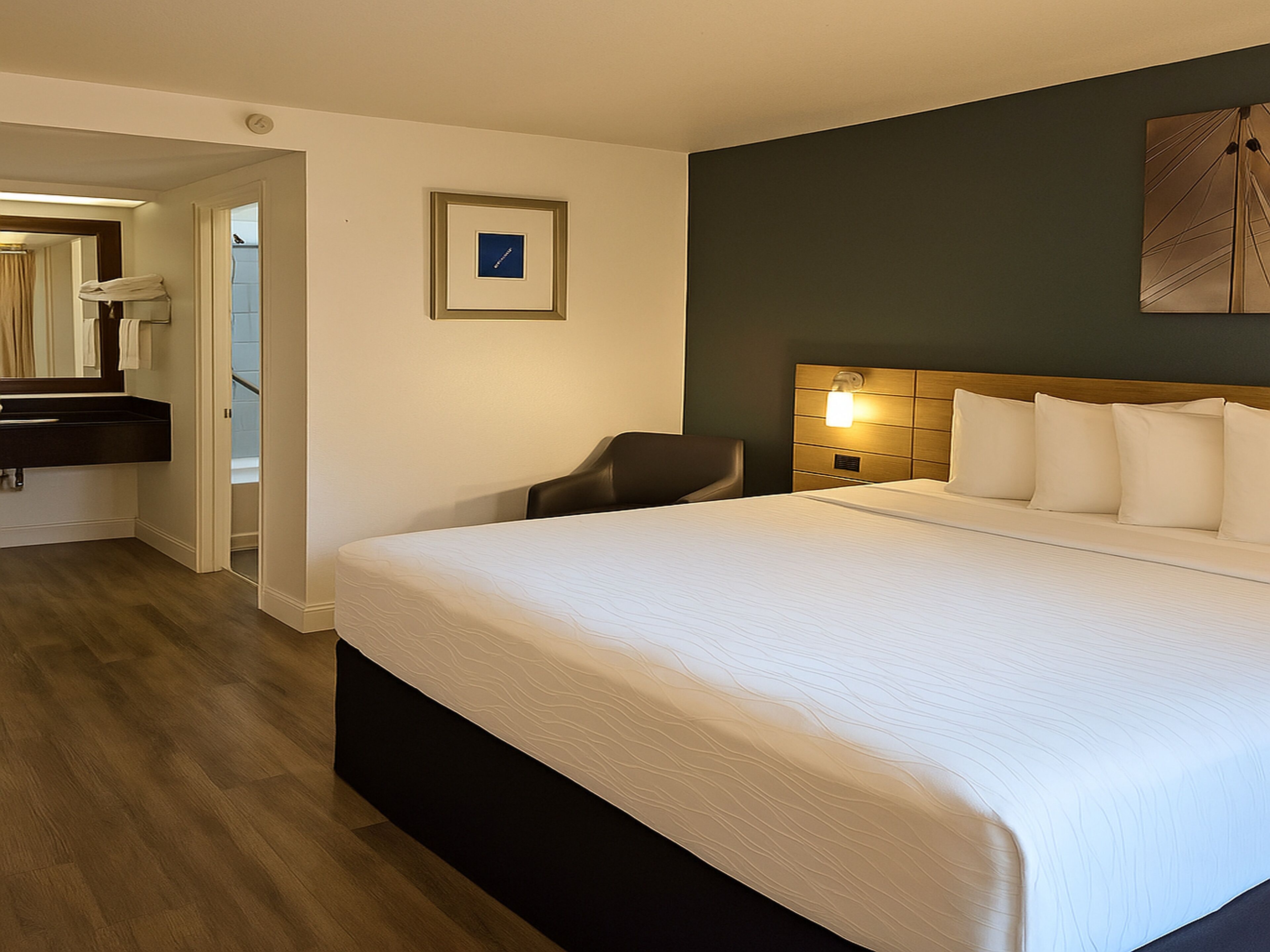 A hotel room with a large bed, a bedside table, a chair, a mirror, and a picture on the wall.