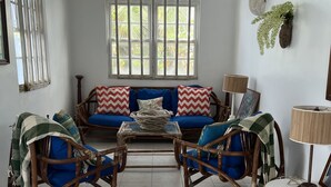 A room with a sofa set, two rocking chairs, a small table, and a window with a view of greenery. - Surfs Up - bungalow style Beachhouse opposite Atlantic Ocean (Bathsheba)
