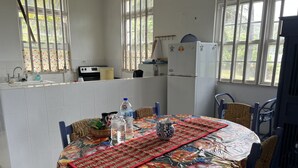 A kitchen with a dining table set for two, a refrigerator, and a window with a view of greenery. - Surfs Up - bungalow style Beachhouse opposite Atlantic Ocean (Bathsheba)