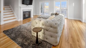 A spacious living room with a large grey sectional sofa, a fireplace, a flat-screen TV, and a ceiling fan. - Stunning Point Pleasant Beach 6BR 5Bath Ocean Front Home - Heated Inground Pool (Point Pleasant Beach)