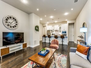 Una sala de estar moderna con una televisión de pantalla plana, una mesa de centro de madera, un sofá y un reloj de pared grande.