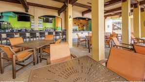 Un área de comedor al aire libre con mesas y sillas de madera, una barra con mostrador verde y una cocina al fondo.