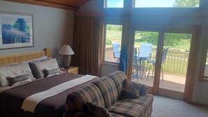 Ein Schlafzimmer mit Bett, Nachttisch, Lampe, einem gerahmten Bild an der Wand und Blick auf eine Terrasse mit Stühlen und Tisch.