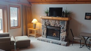 Ein gemütliches Wohnzimmer mit Kamin aus Stein, einem Fernseher auf einer hölzernen Konsole und einer Wanddekoration mit Kaffeemotiv.