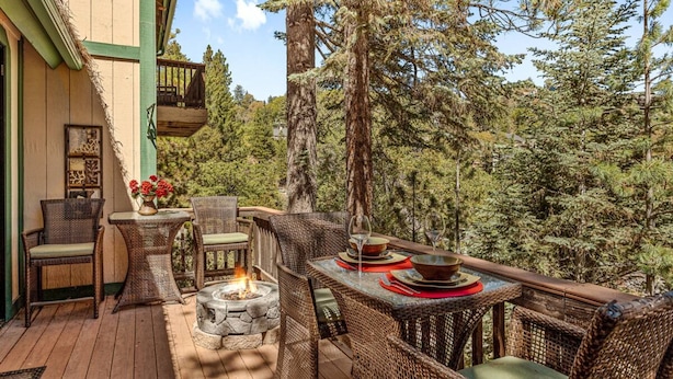 Una terraza exterior con mobiliario de mimbre, un hogar de piedra y una mesa de comedor preparada para dos personas.