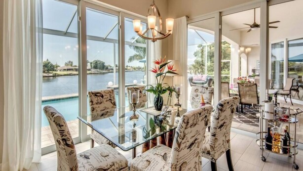 A spacious dining area with a glass table, patterned chairs, and a view of a lake. - Villa Blissful Bay - The Entry To Paradise (Cape Coral)
